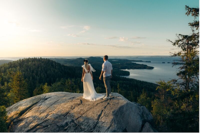 Paar in Hochzeitskleidung steht auf einem Felsen über einem See