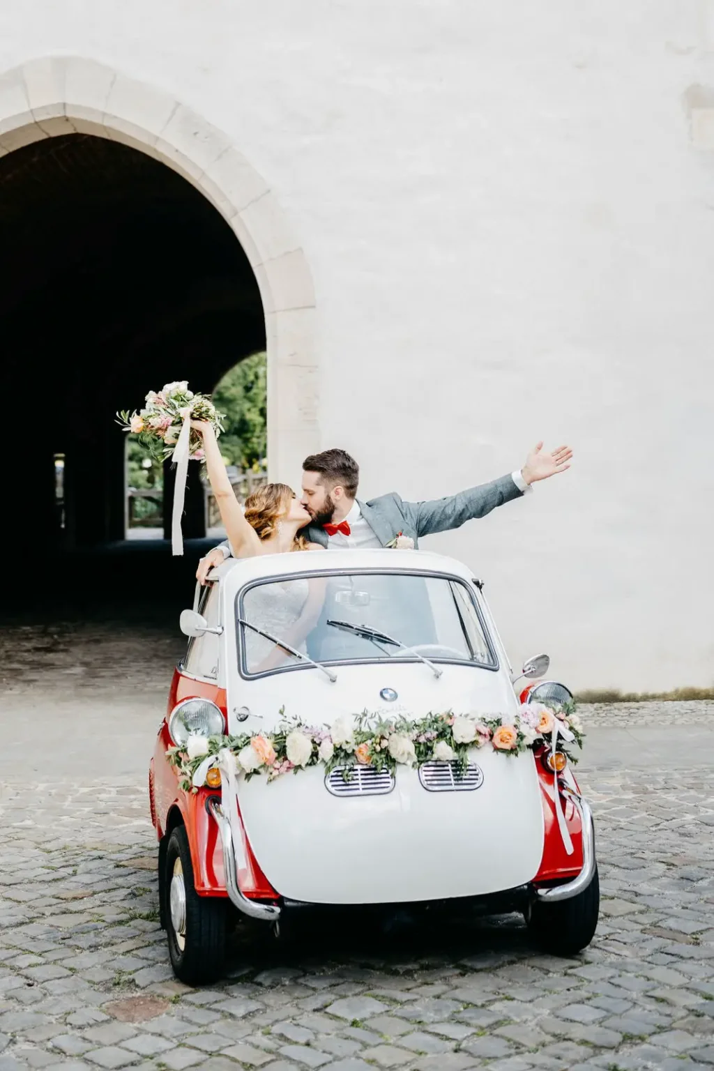 Zwei Personen winken aus einem blumengeschmückten Kleinwagen