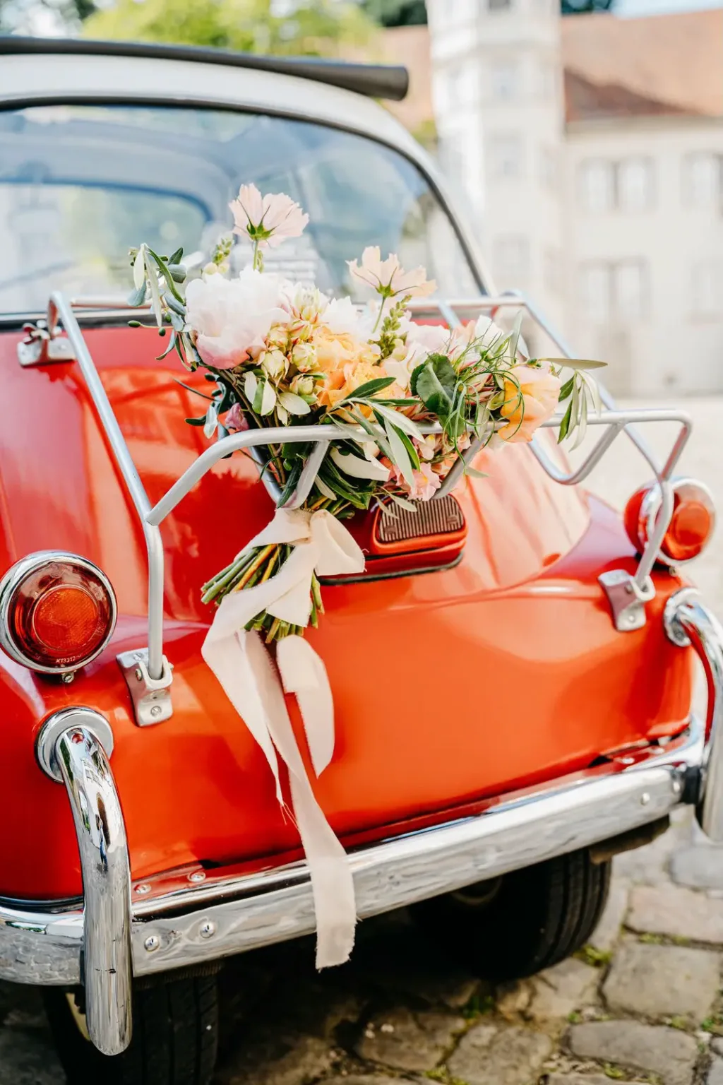 Heck eines roten Kleinwagens mit Blumen und weißen Bändern
