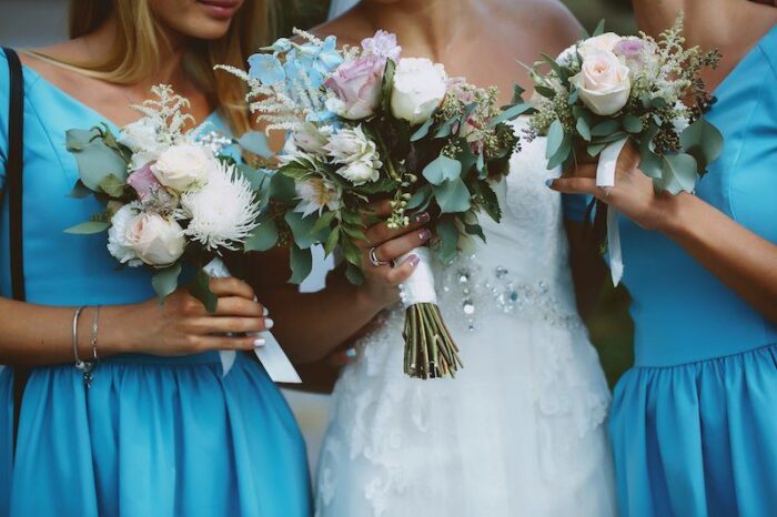 Braut und Begleiterinnen halten weiße und hellblaue Blumensträuße