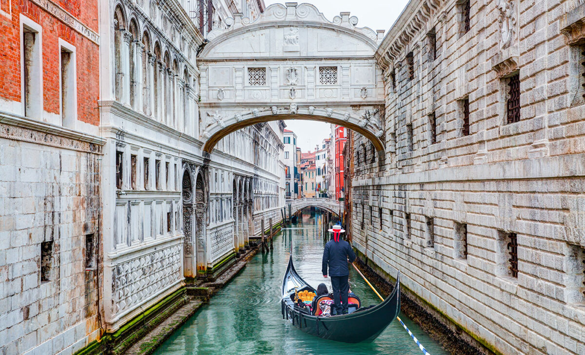 Honeymoon Horoskop: Eine Gondel gleitet durch die engen Kanäle von Venedig, Italien, mit Bögen und historischen Gebäuden im Hintergrund.
