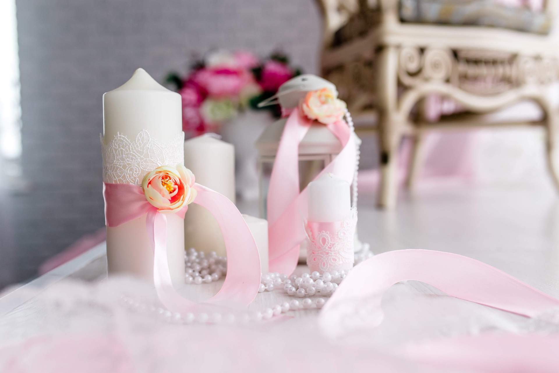 Drei weiß-rosafarbene Hochzeitskerzen mit Bändern und Blüten