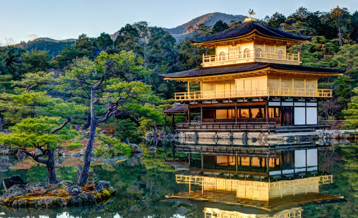 Honeymoon Horoskop: Der Goldene Pavillon von Kyoto in Japan mit seiner Spiegelung im Wasser, umgeben von grünen Bäumen und Bergen.