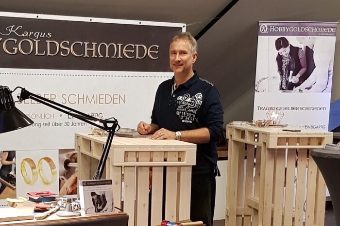 Goldschmied an einem Messestand für selbst geschmiedete Trauringe