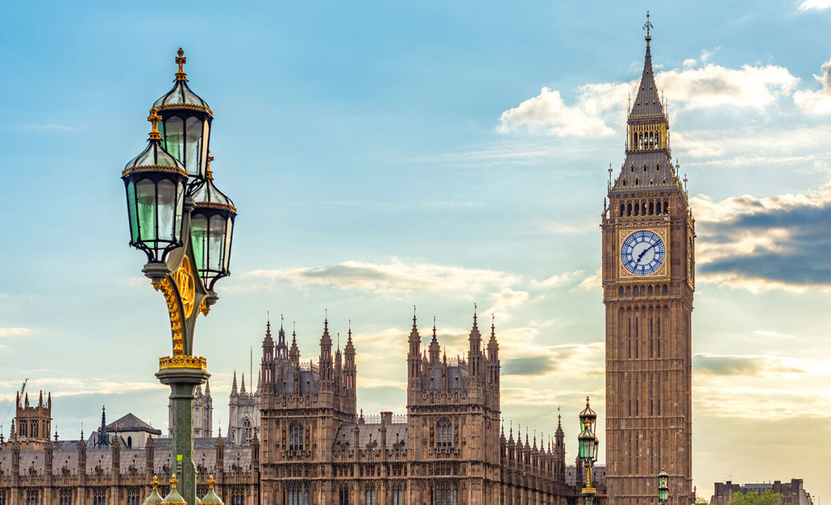 Big Ben und die Houses of Parliament in London, Vereinigtes Königreich. Blick von der Steinbrücke mit einer Straßenlaterne und dem Glockenturm an einem sonnigen Tag.