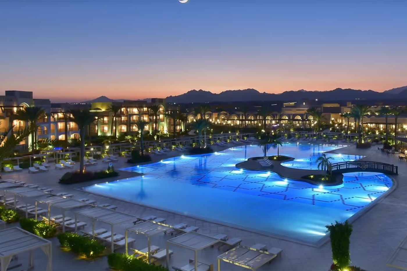 Großer Hotelpool vor beleuchteten Gebäuden in der Dämmerung