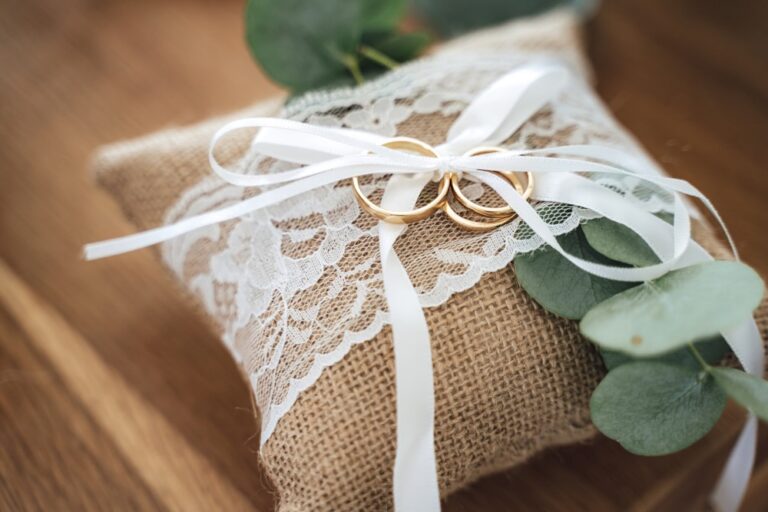 Set aus drei goldenen Ringen auf einem kleinen Jutekissen, verziert mit weißer Spitze und Schleife;Hintergrund aus Holz;Motiv: Hochzeitstag