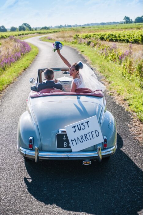 Brautpaar im hellblauen Oldtimer auf einer Landstraße mit Just-Married-Schild am Heck.
