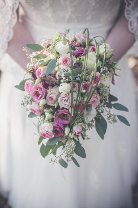 Hängender Blumenstrauß in Rosa und Violett vor einem Brautkleid